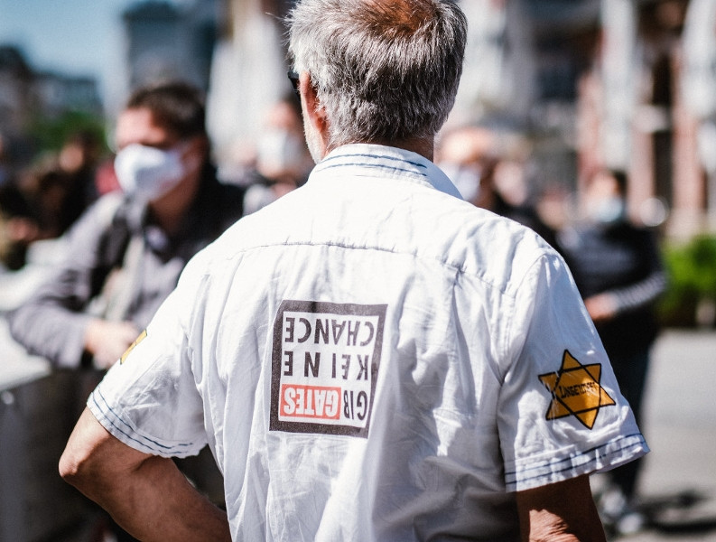 Ein weiterer Aspekt des Antisemitismus besteht in der Relativierung der Shoah, die von Teilnehmenden der Proteste gegen die Maßnahmen wegen der COVID-19-Pandemie vorgetragen wird. So kennzeichneten sich einige Impfgegner*innen mit dem Judenstern um sich zu Opfern von Verfolgung zu stilisieren. Das Bild zeigt einen Teilnehmer einer Demonstration gegen die Corona-Maßnahmen im Mai 2020 in Frankfurt am Main.