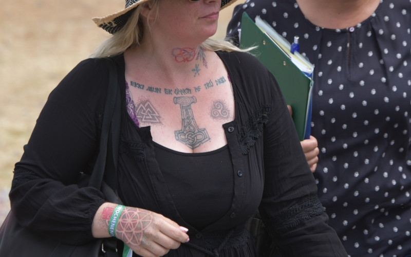 Als Tätowierungen dieser Teilnehmerin eines Neonaziskonzertes 2019 sind zu erkennen: Die Valknut, der Thorshammer und die gerundete Triskele.