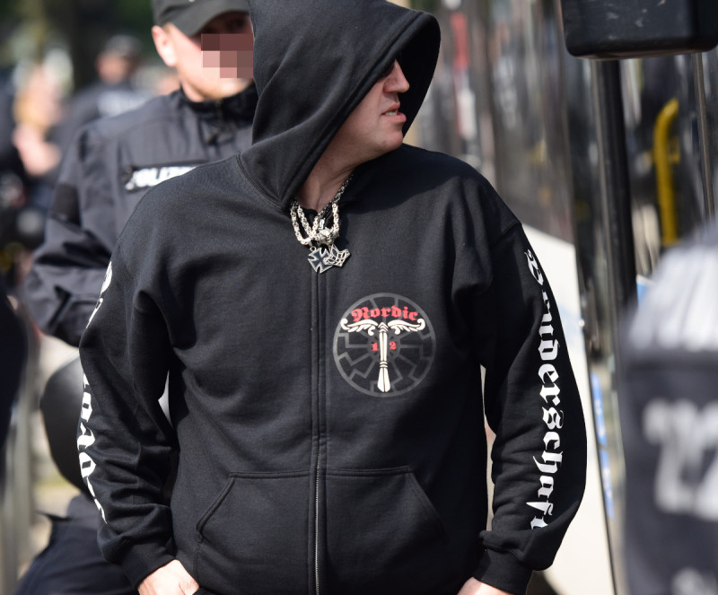 In der Zurschaustellung von Symbolen verbinden Neonazis sehr häufig Bezüge auf das Germanentum / Heidentum und auf den Nationalsozialismus. Das Bild zeigt einen Angehörigen der Neonazigruppe Nordic 12 mit Thorshammer, Eisernem Kreuz, Schwarzer Sonne und NS-Irminsul.