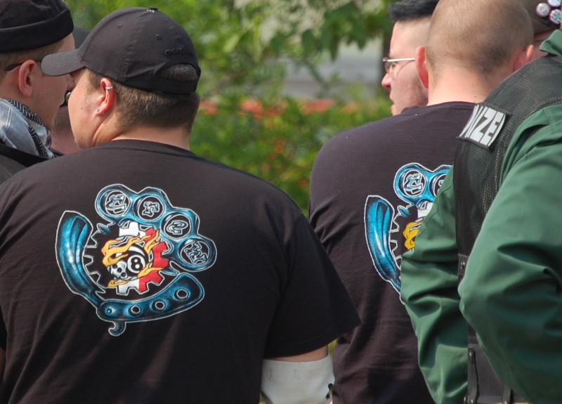 »Crew 38«-Erkennen für Fortgeschrittene. "Crew" steht in den Finger-Löchern des abgebildeten Schlagrings.Die »38« ist durch einen Würfel mit der 3 und eine Billardkugel mit der 8 (»Eightball«) dargestellt. Jedoch: Das schwarz-weiß-rote Zahnrad ist ein typisches Erkennungmerkmal von Hammerskins.